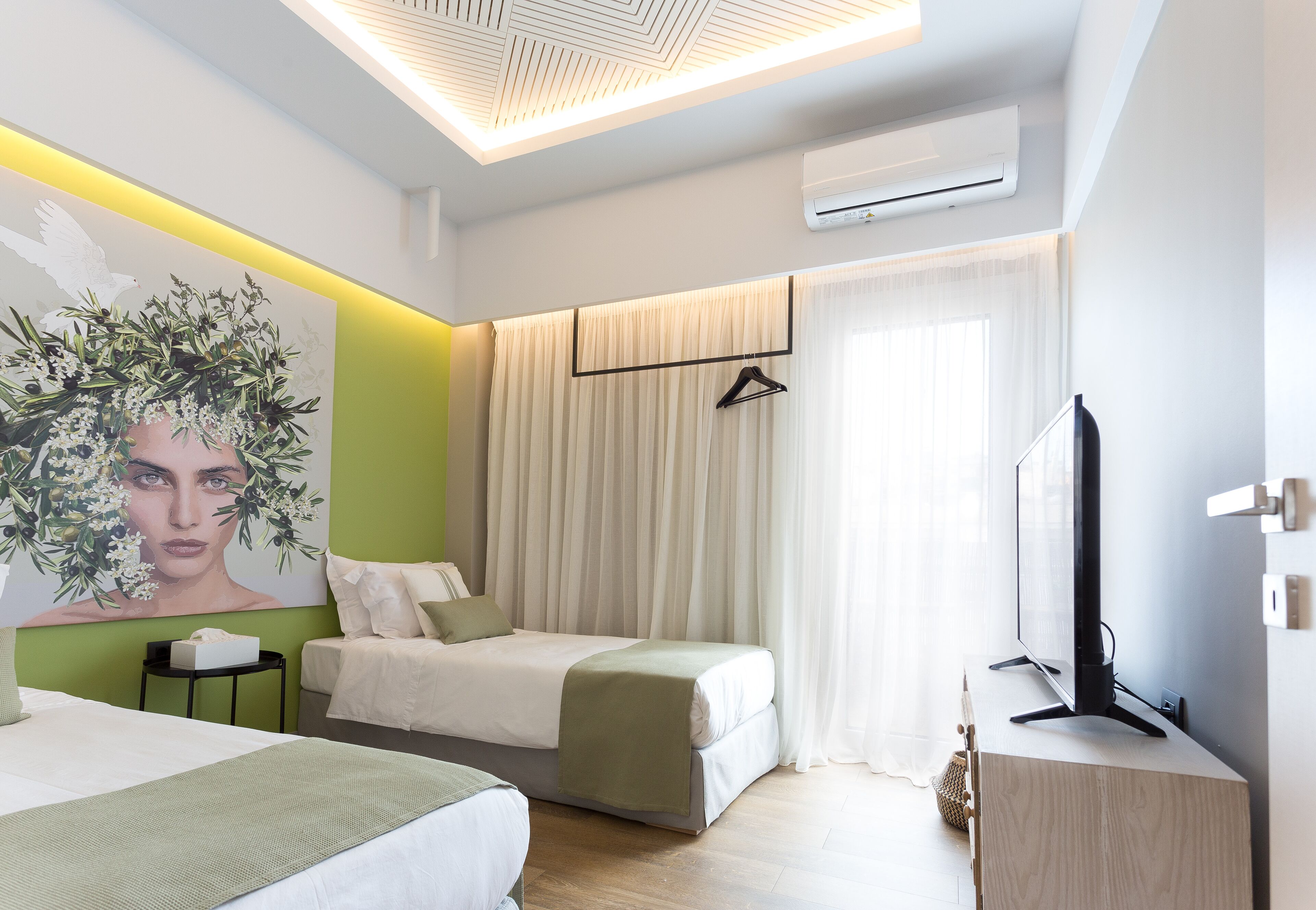 A modern hotel room with two beds, a flat-screen TV, a small table, and a painting on the wall.