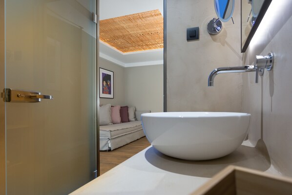 A modern bathroom with a large white vessel sink, a shower with a bamboo ceiling, and a minimalist design. - Artree Suites (Heraklion)