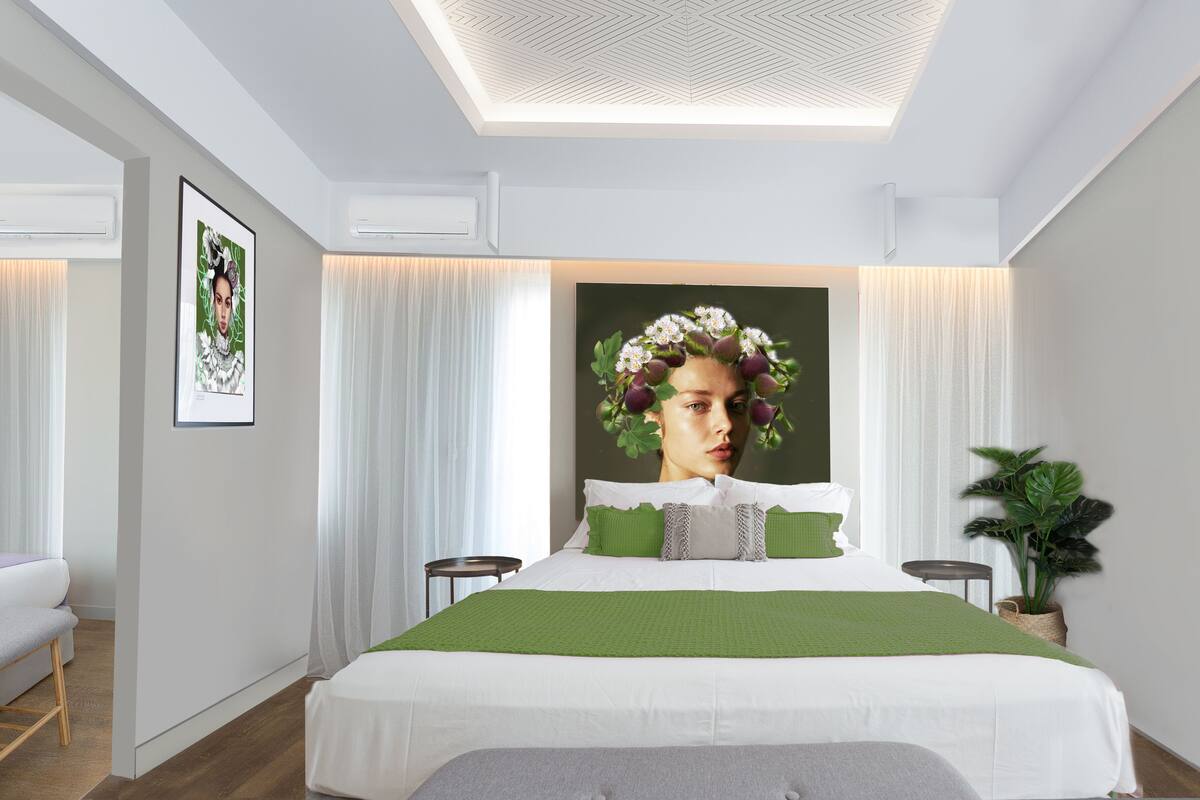 A modern bedroom with a large bed, a green throw, and a large floral artwork on the wall.