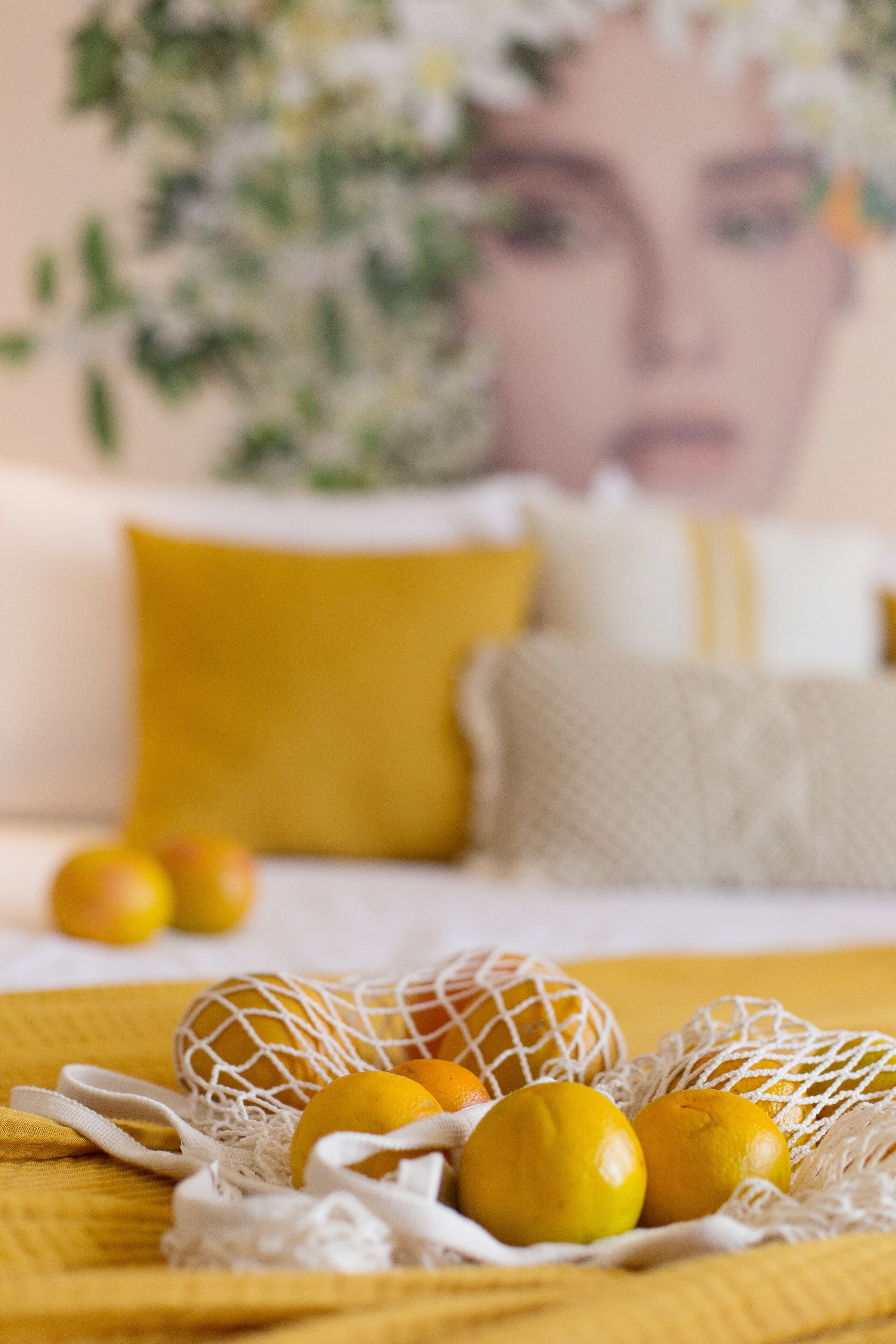 A bed with a yellow pillow and a white net bag containing oranges and lemons on a yellow bedspread.