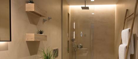 A modern bathroom with a large sink, a toilet, a shower, and a mirror. There are wooden shelves with plants and a ladder for hanging towels.