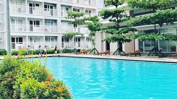 Un hôtel à plusieurs étages doté d’une piscine entourée de verdure et de coins salons extérieurs.