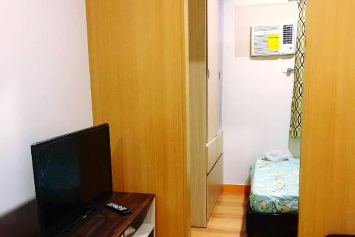 Une pièce de taille modeste, comprenant un bureau en bois, un lit et un petit coin cuisine.