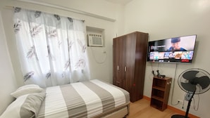 Une chambre avec un lit, une armoire, une télévision et un ventilateur.
