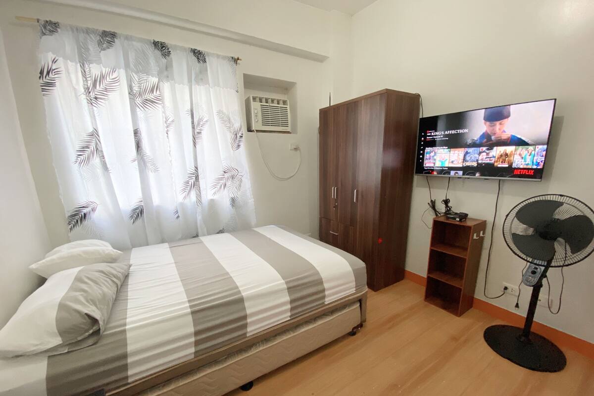 Une chambre avec un lit, une armoire, une télévision et un ventilateur.