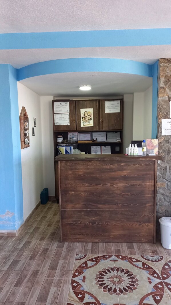 A reception desk with wooden panels, certificates on the wall, and a patterned rug on the floor. - ADA KEKİĞİ PANSİYON (Gökçeada)