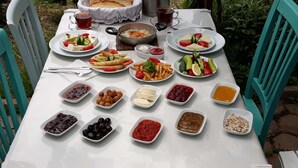 A table set outdoors with various dishes, including salads, bread, and a pot of rice. - ADA KEKİĞİ PANSİYON (Gökçeada)
