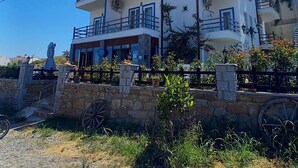A multi-story building with balconies, a stone wall in front, and a clear blue sky. - ADA KEKİĞİ PANSİYON (Gökçeada)