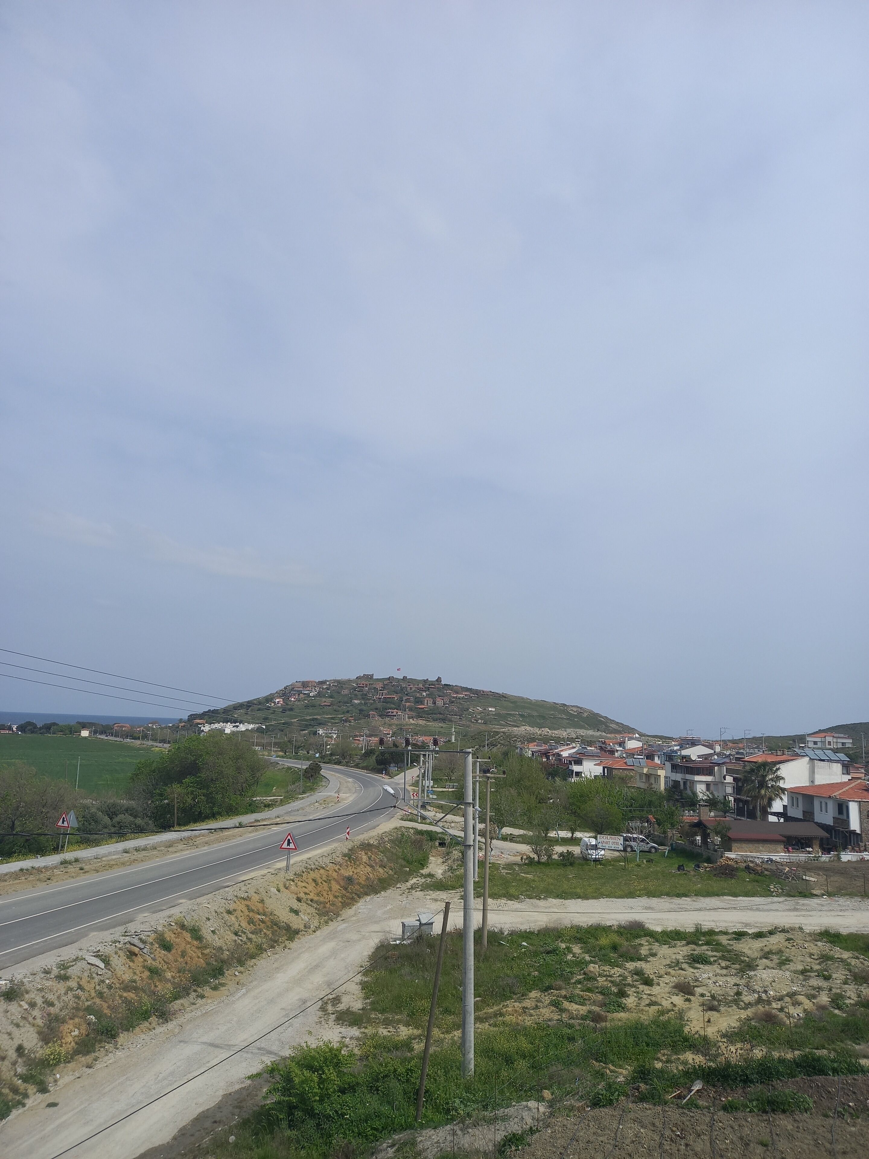 Un camino rural con una curva, una colina con edificios y un cielo despejado.