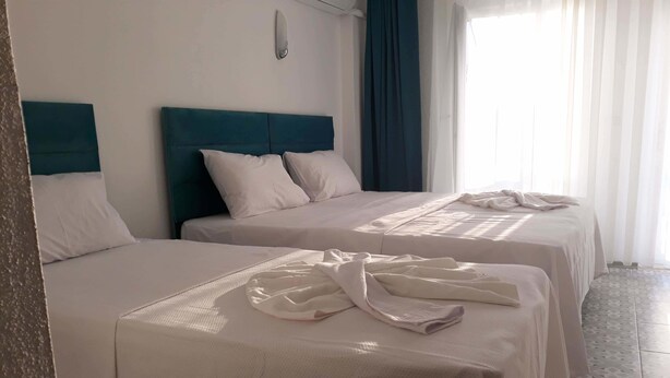 Two twin beds with white linens and a blue headboard, a bathroom with a white sink and mirror, and a patterned floor. - ADA KEKİĞİ PANSİYON (Gökçeada)