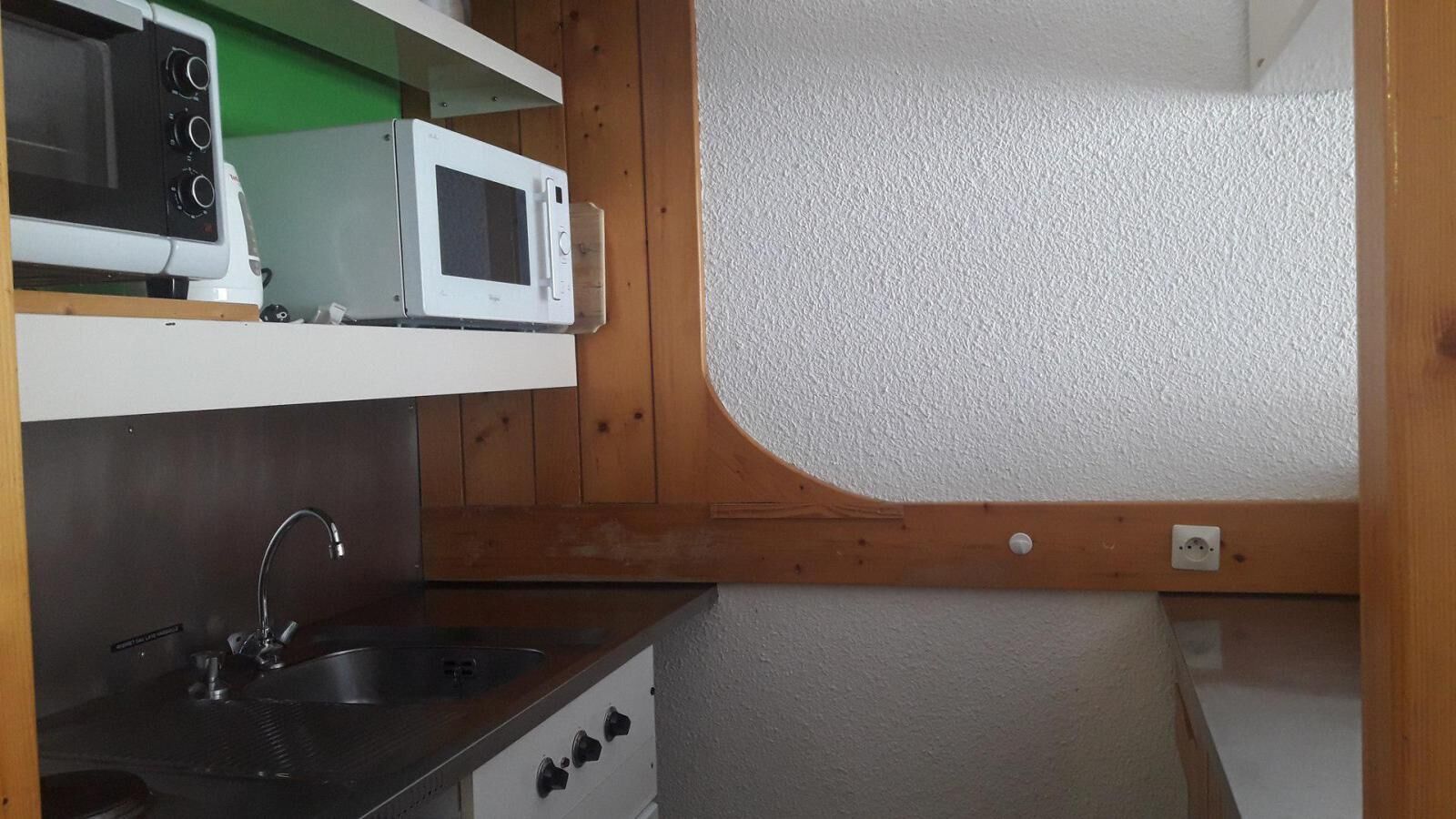 Een kleine keuken met een magnetron, spoelbak en fornuis.
