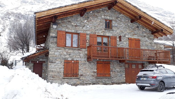 Un bâtiment en pierre doté de balcons en bois, avec une voiture garée devant.