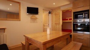 Une table à manger en bois avec des bancs, un téléviseur à écran plat fixé au mur et un four encastré avec fonction micro-ondes.