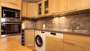 Une cuisine moderne avec des meubles en bois, un évier en acier inoxydable, un lave-vaisselle Bosch et un lave-linge.