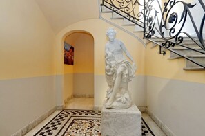 A marble statue in a hallway with a tiled floor and a staircase with ornate metal railings. - Cozy Vittoria Colonna (Rome)
