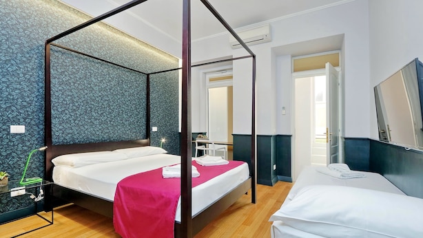 Un lit à baldaquin avec du linge de lit blanc et une touche de rose, une table de chevet avec une lampe, et un grand miroir au mur.