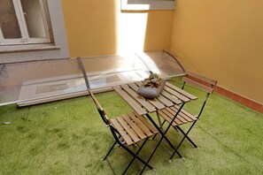 A small patio area with a wooden table and chairs, a potted plant, and a window with a view of the outside. - Cozy Vittoria Colonna (Rome)