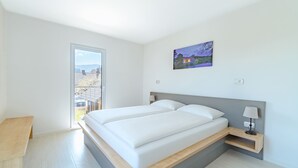 A modern bedroom with a large bed, a bedside table, a nightstand, and a painting on the wall.