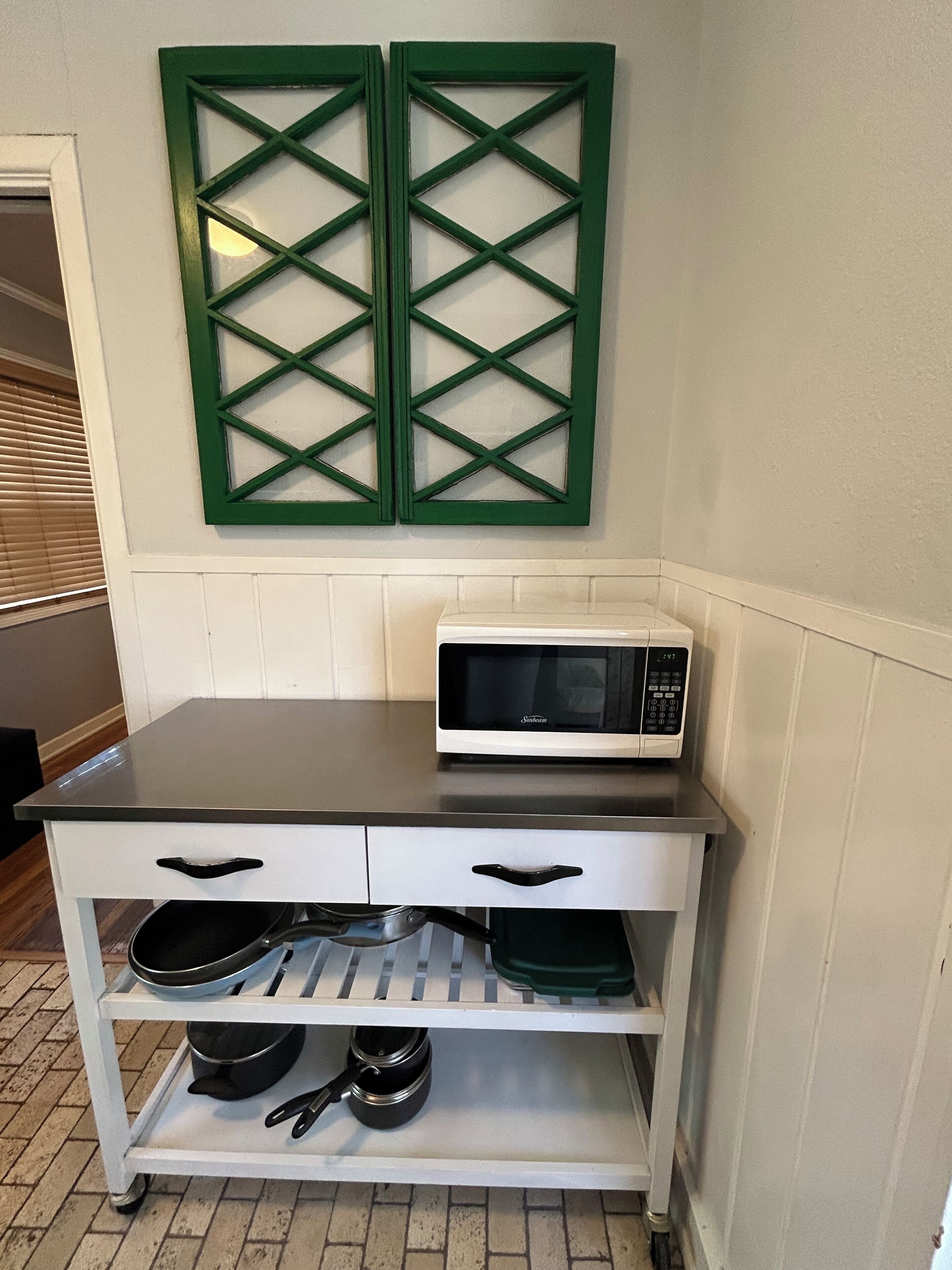 A kitchen counter with a microwave, a white cabinet with drawers, and a green decorative panel above.