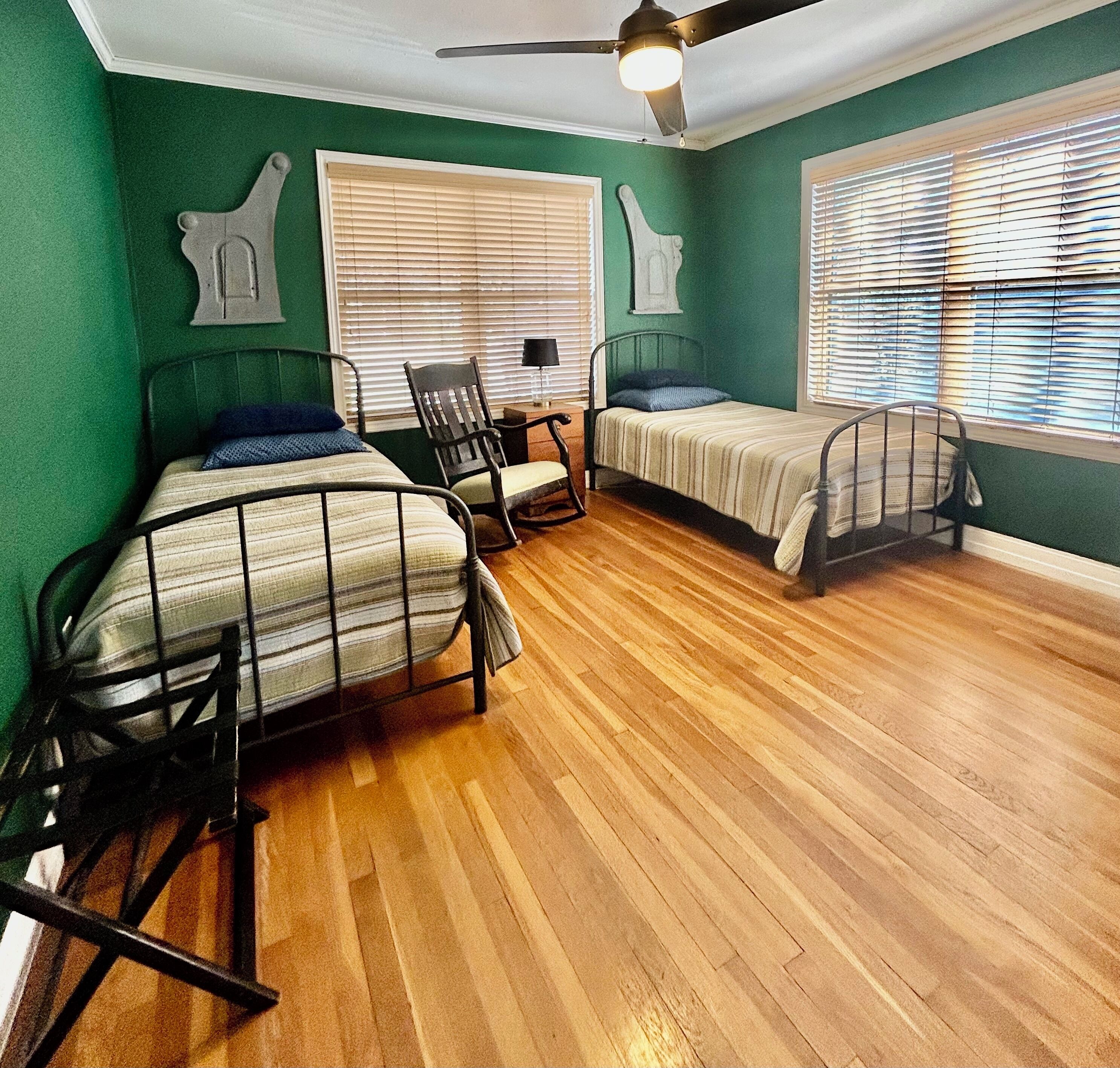 A room with two metal bunk beds, a ceiling fan, and a window with blinds.