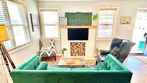 Ein Wohnzimmer mit einem grünen Sofa, einem Kamin, einem Fernseher und Holzboden.