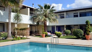 Area piscina con una palma, piante in vaso e un edificio con numerosi balconi.