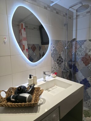 A bathroom with a modern sink, a shower with a handheld showerhead, and a decorative mirror.