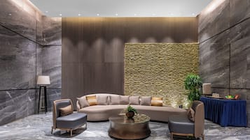 A modern lounge area with a curved sofa, two armchairs, a coffee table, a lamp, and a small table with a plant.