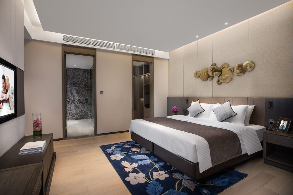 A modern hotel room with a large bed, a built-in wardrobe, a flat-screen TV, and a decorative wall piece.