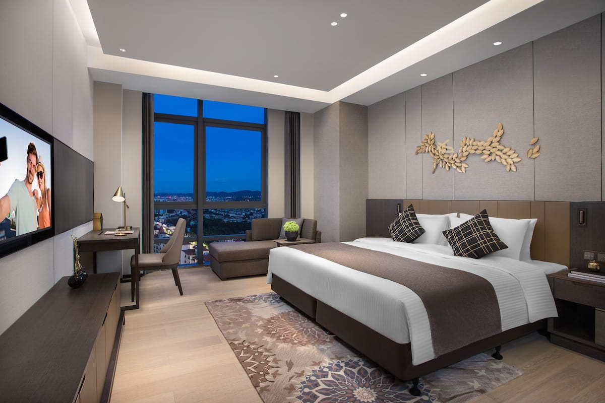 A modern hotel room with a large bed, a desk, a chair, and a TV.