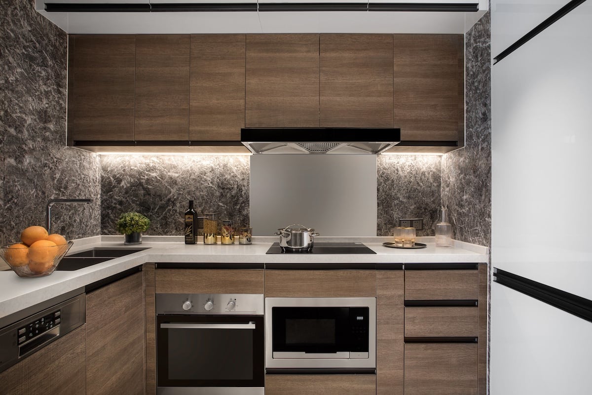 A modern kitchen with dark wooden cabinets, a stainless steel oven, a microwave, and a black range hood.