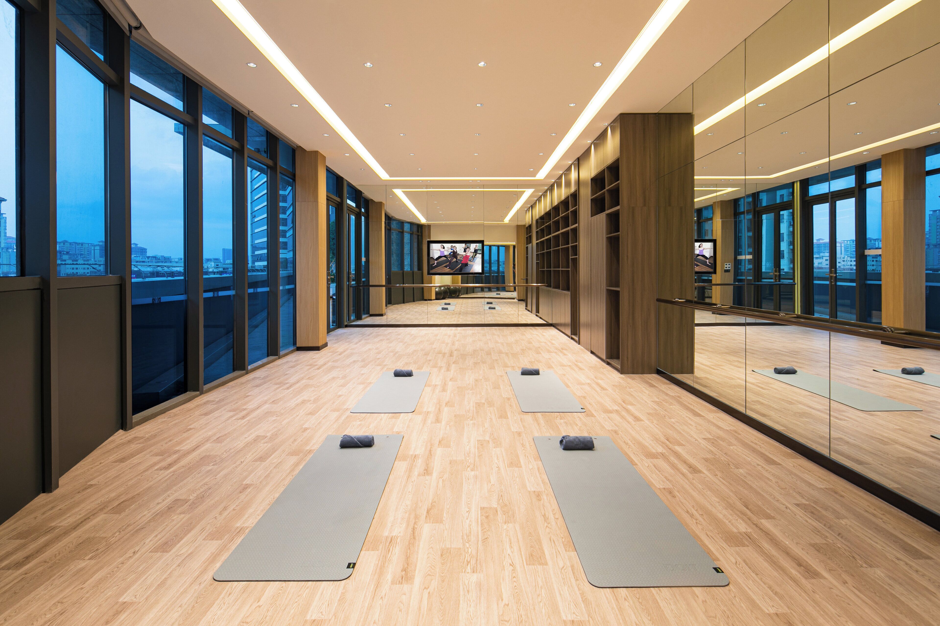 Quarto espaçoso com grandes janelas, televisão de tela plana e tapetes de yoga dispostos no chão.