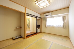 A traditional Japanese room with tatami flooring, a sliding door, a small shelf, and an air conditioning unit. - Tabist Annex Matsumi (Beppu)
