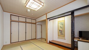 Ein traditioneller japanischer Raum mit Tatami-Boden, Schiebetüren, einem Fernseher und einem kleinen Schrank.