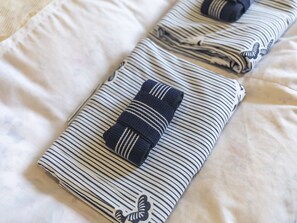 A neatly folded towel with a striped pattern and a small embroidered butterfly on a bed. - Tabist Annex Matsumi (Beppu)