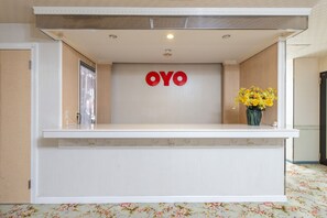 A reception desk with a "OYO" sign, a vase with yellow flowers, and a floral carpet. - Tabist Annex Matsumi (Beppu)