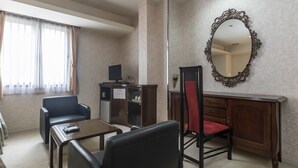 Ein Hotelzimmer mit Schreibtisch, zwei Stühlen, einem kleinen Tisch, einem Spiegel und einem Fenster mit Vorhängen.