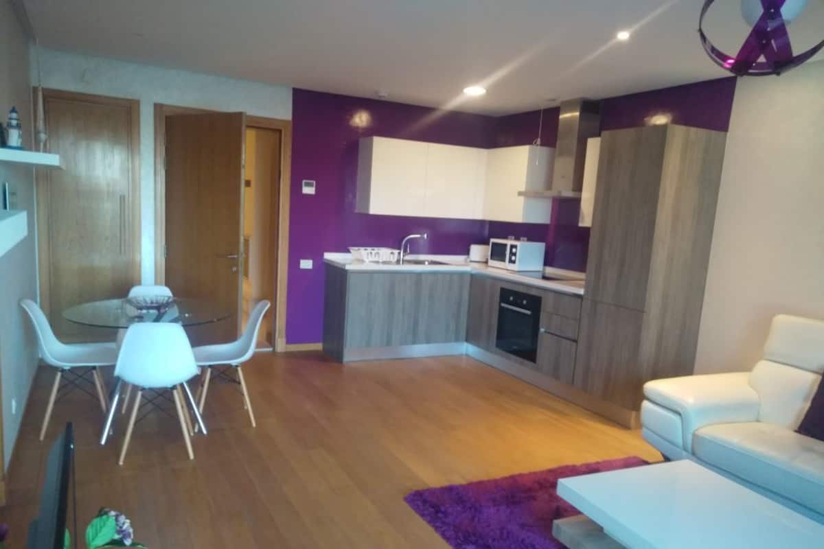 Una sala de estar moderna con un sofá blanco, una mesa de comedor con sillas blancas y una zona de cocina con microondas y estufa.