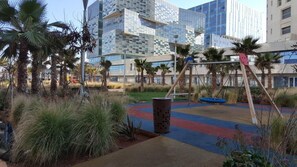 Un’area giochi colorata, palme e edifici moderni sullo sfondo.