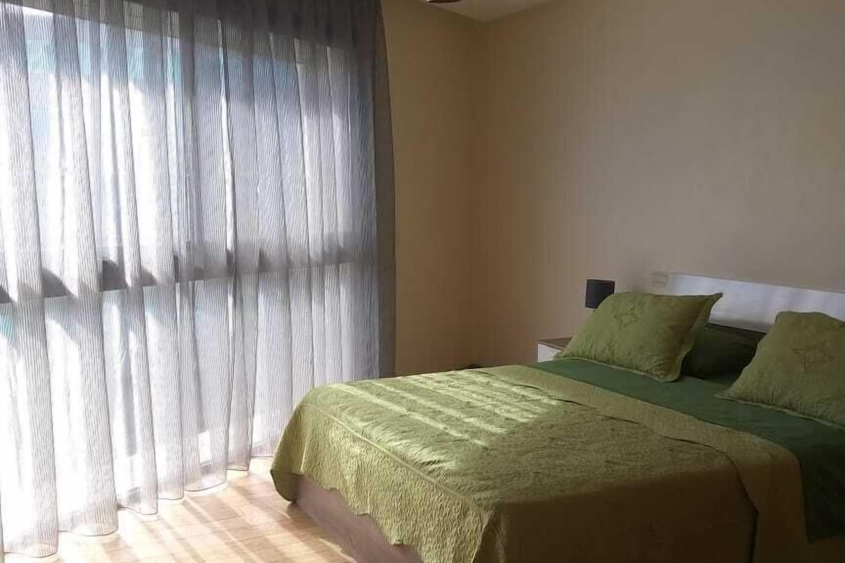 Un dormitorio con cama, cortinas, lámpara colgante y suelo de madera.