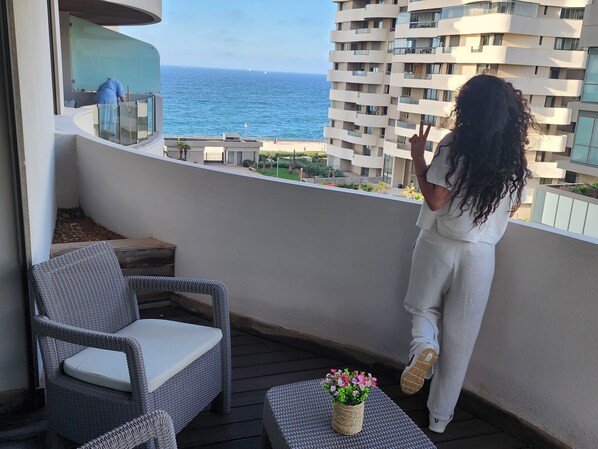 Un balcone con mobili in vimini, una pianta in vaso e vista sull'oceano e sugli edifici.