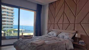 A modern bedroom with a large bed, a view of the sea, and a geometric wall design. - Marina Casablanca by Saloua (Casablanca)
