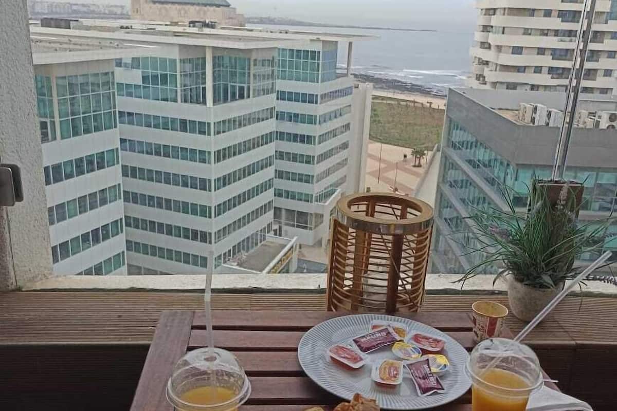Desayuno en un balcón con vista a la ciudad, incluyendo una torre de reloj y edificios modernos.