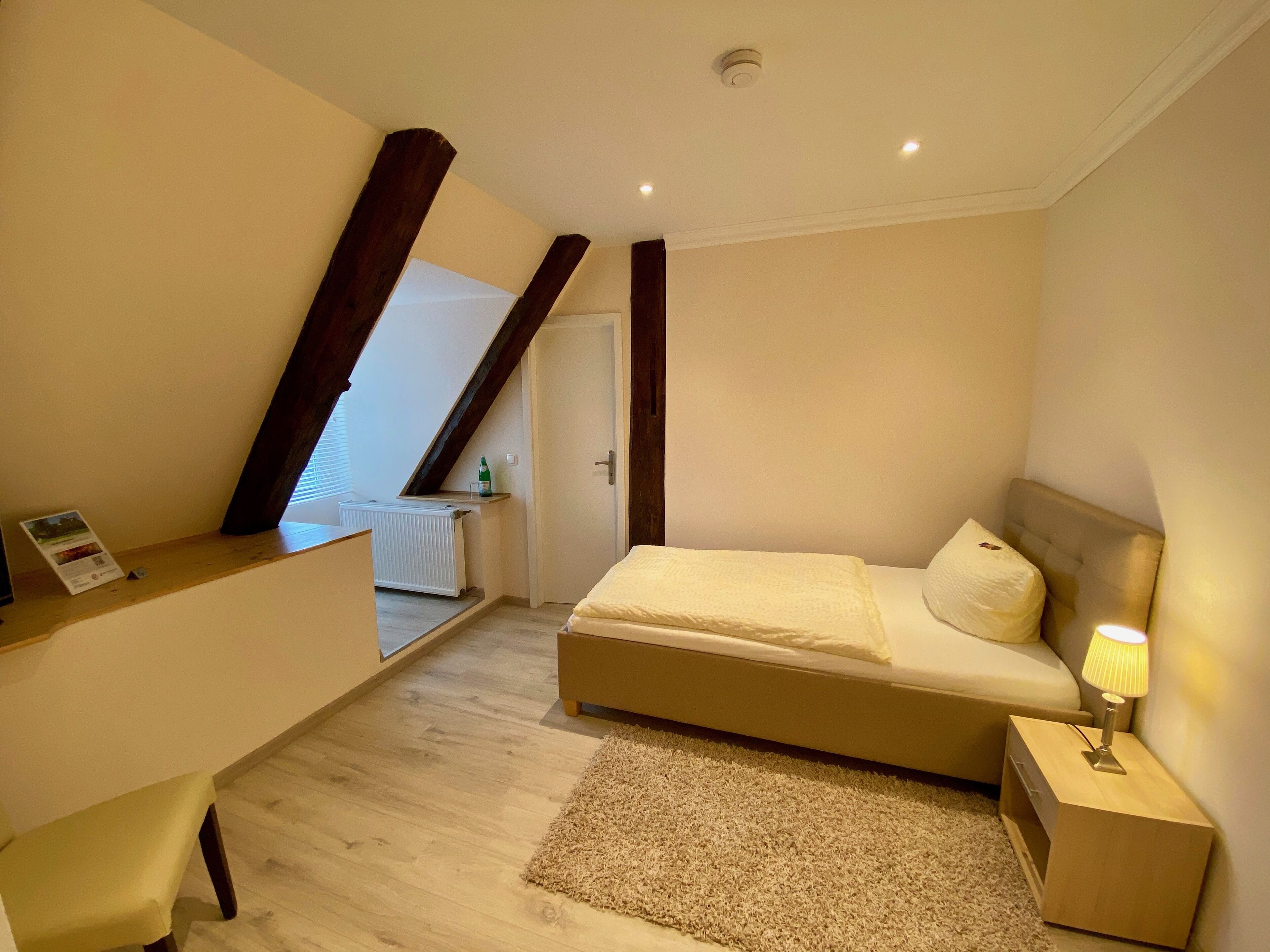 A bedroom with a bed, a nightstand, a lamp, a radiator, and a window with blinds.