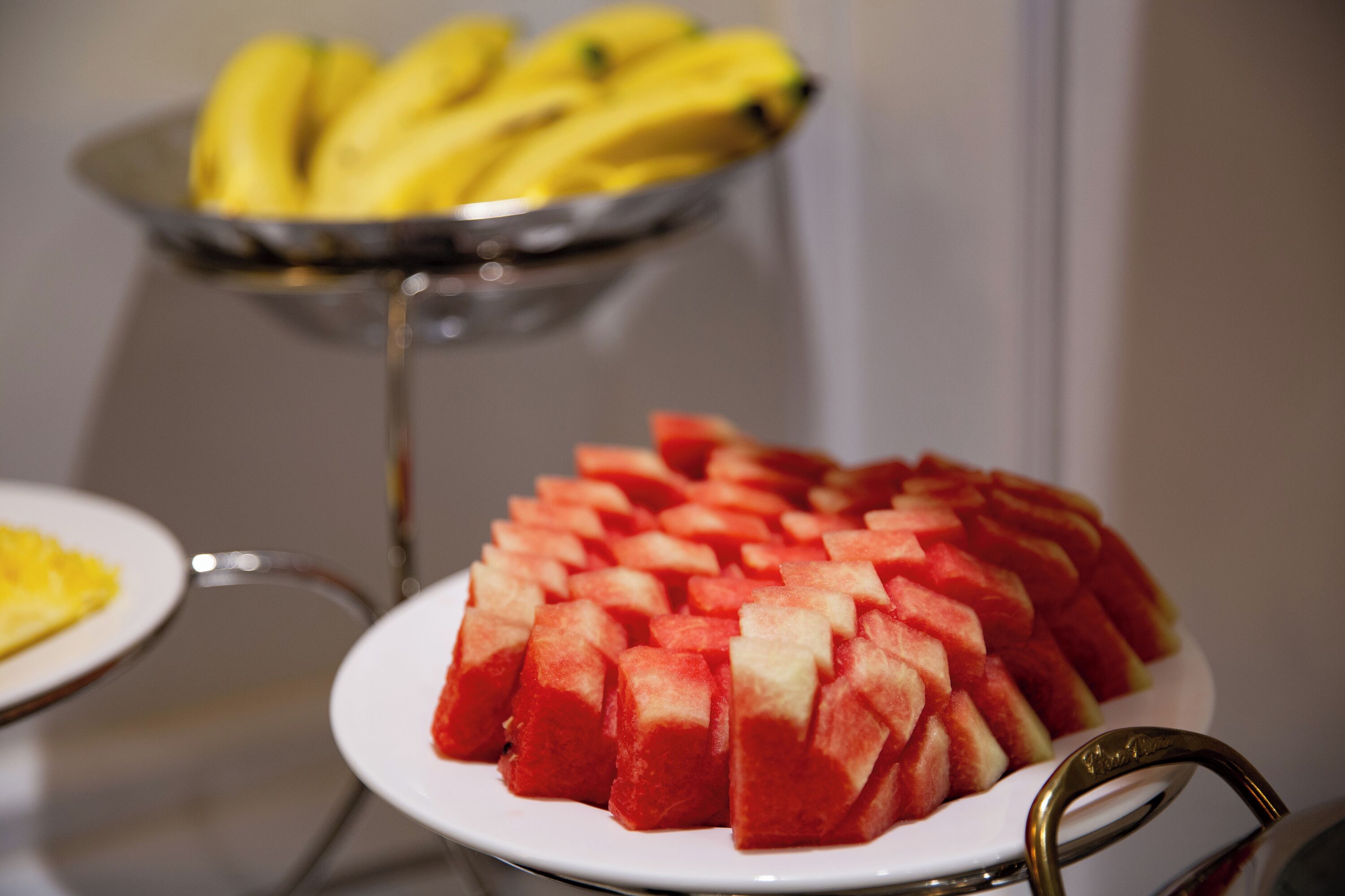 A table with a plate of cubed watermelon and a bowl of bananas.