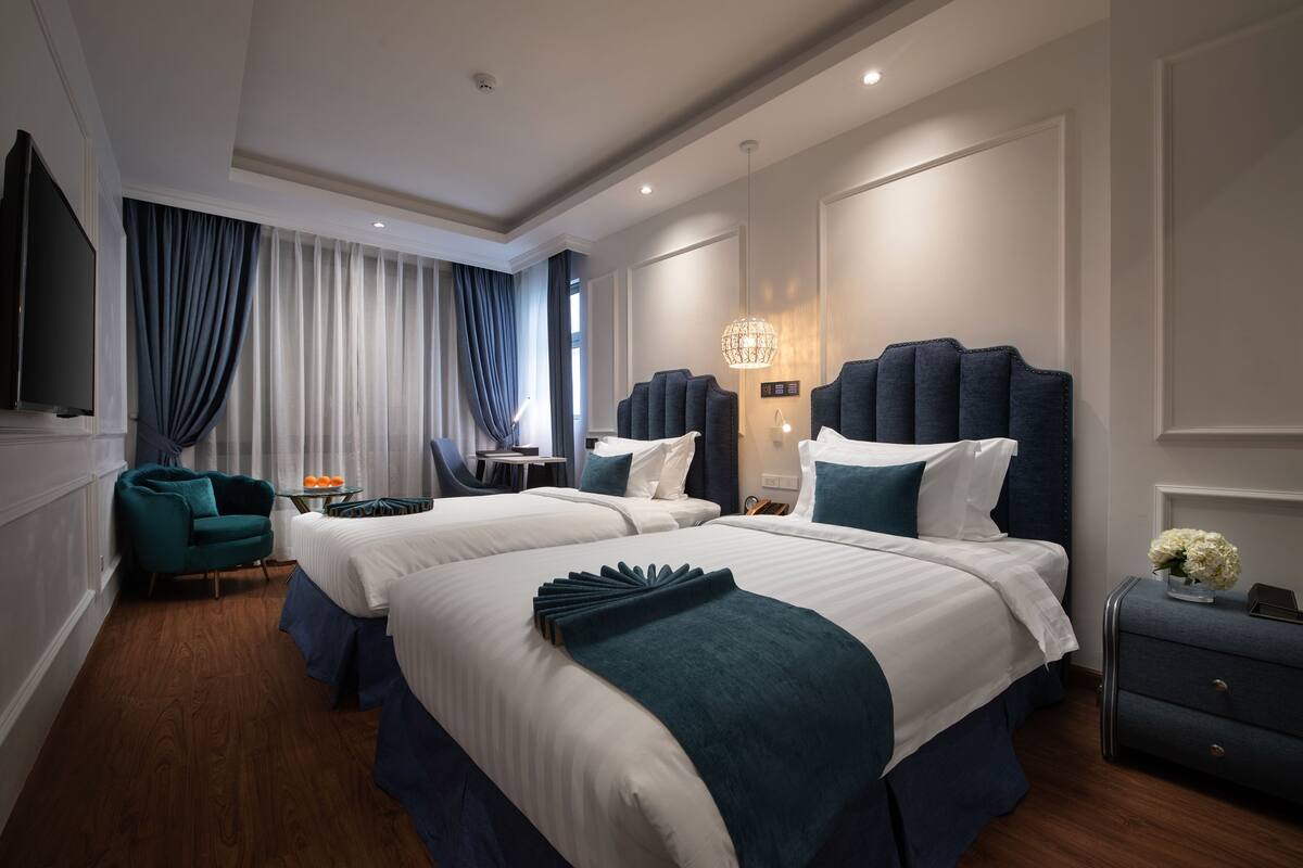 A modern hotel room with two beds, a TV, a desk, and a chair.