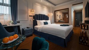 Una moderna camera d'albergo con un grande letto, comodini, una scrivania con una sedia, un tavolino con arance e un ampio specchio.