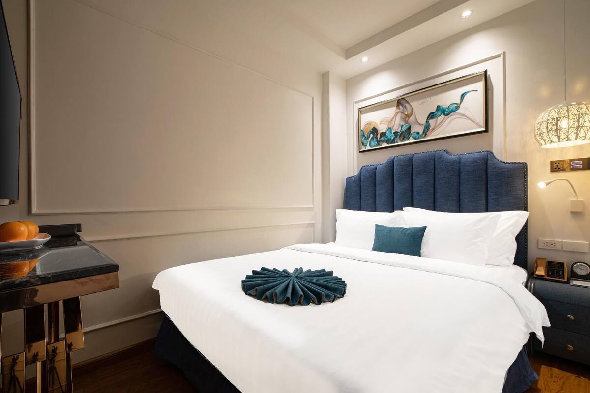 A neatly made bed with a white and blue headboard, a decorative pillow, and a wall-mounted artwork above it.