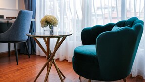 Una stanza con una poltrona verde acqua, un tavolino rotondo con base dorata e un vaso di fiori.