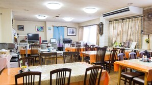 Un comedor con varias mesas y sillas, un televisor y una kitchenette.
